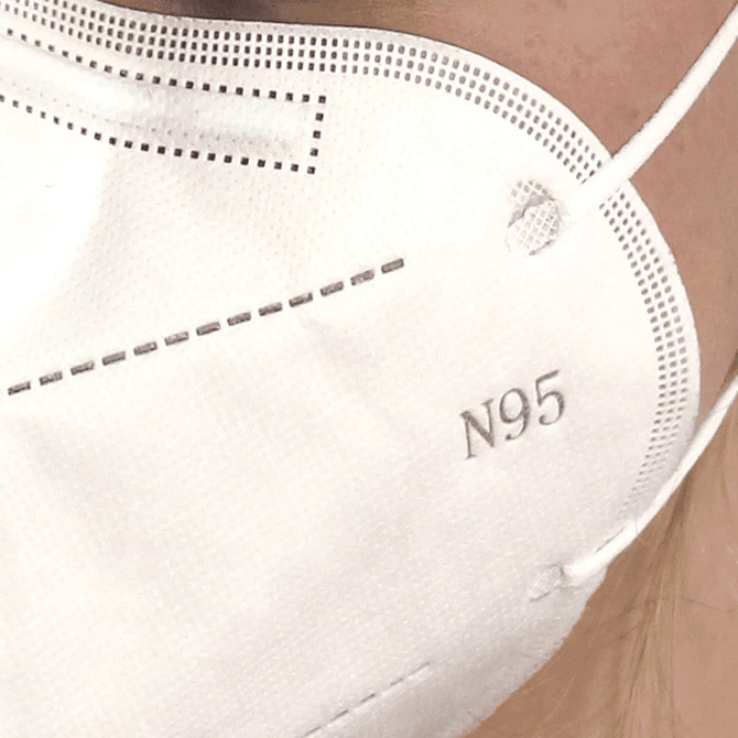 A close-up of a white N95 respirator face mask, featuring a branded logo and a textured surface.