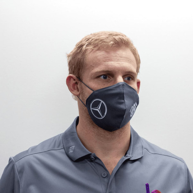 A grey face mask with a logo, worn by a person, featuring ear loops for a secure fit.