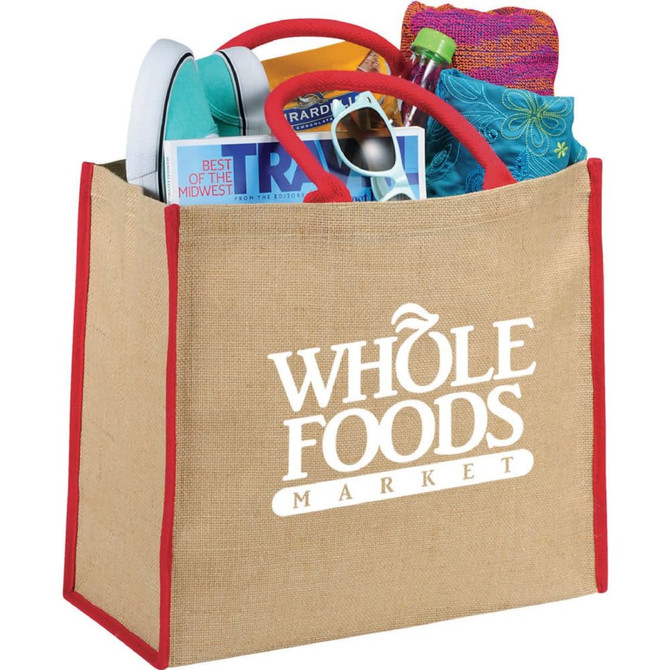 A large jute tote bag in natural with red handles, filled with books, a drink bottle, and other items.