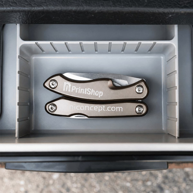 A silver multi-tool featuring several tools, placed inside a grey storage compartment. The tool has a branded logo.