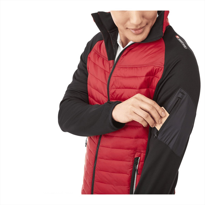A man wearing a red and black insulated jacket, featuring a zippered pocket on the arm and a logo.
