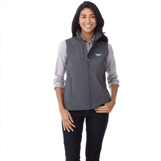 A woman wearing a grey softshell vest, featuring a logo, with a button-up shirt underneath.