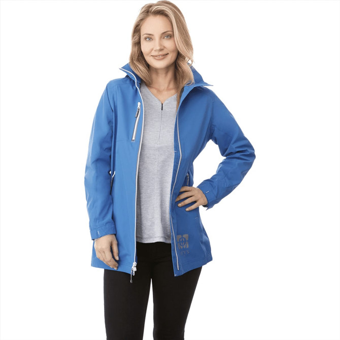 A woman in a blue rain jacket with a hood, paired with a grey top and black trousers, smiling at the camera.