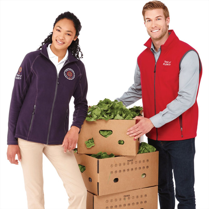 A purple women's polyfleece jacket and a red vest are worn by a man and a woman next to boxes of lettuce.