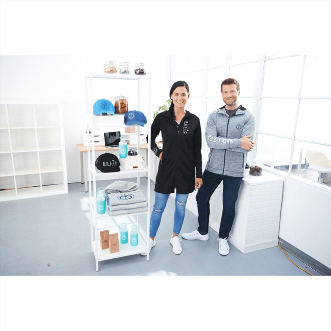 A woman in a black shirt and a man in a grey zip hoodie stand beside a display of various products, including caps and bottles.