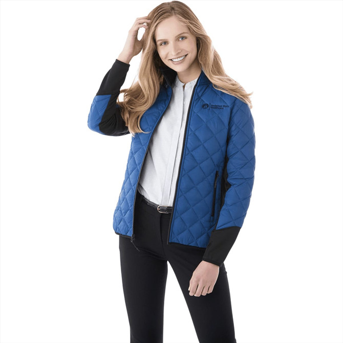 A woman wearing a blue quilted hybrid insulated jacket with black sleeves and a logo.