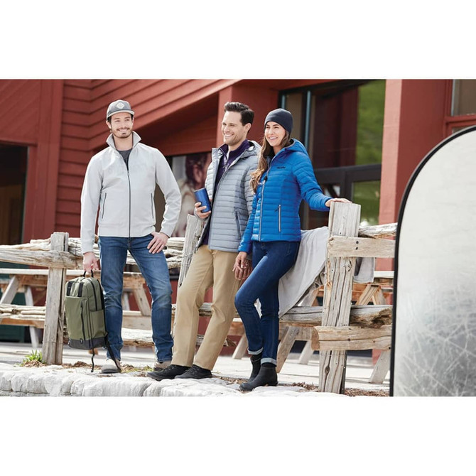 A group of three people wearing jackets, including a blue insulated one, in a rustic outdoor setting.