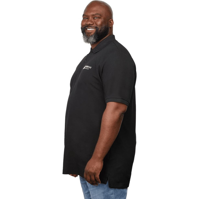 A man in a black polo shirt with a logo, standing with a smile and facing left. The shirt has a longer cut.