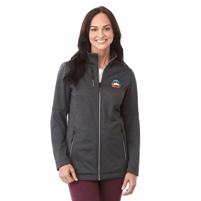 A woman wearing a charcoal grey softshell jacket with a logo on the chest and zippered pockets.