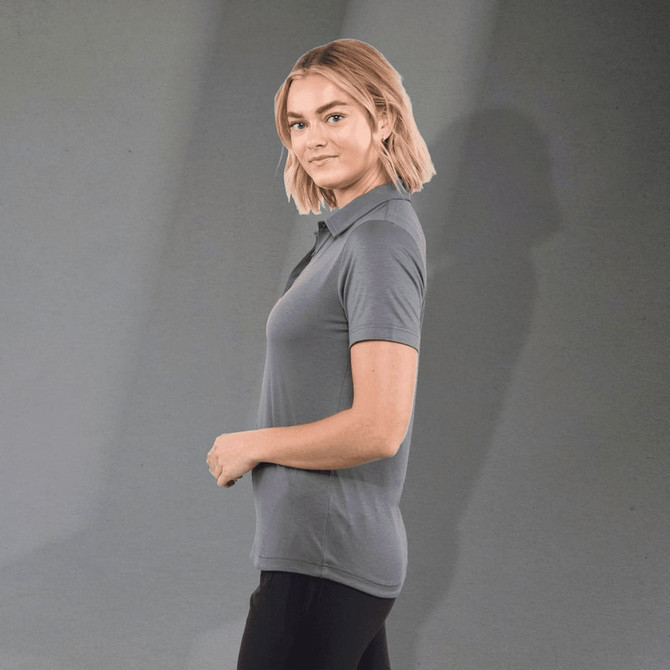 A grey women's polo shirt featuring a classic design and a logo. The model is standing facing sideways.