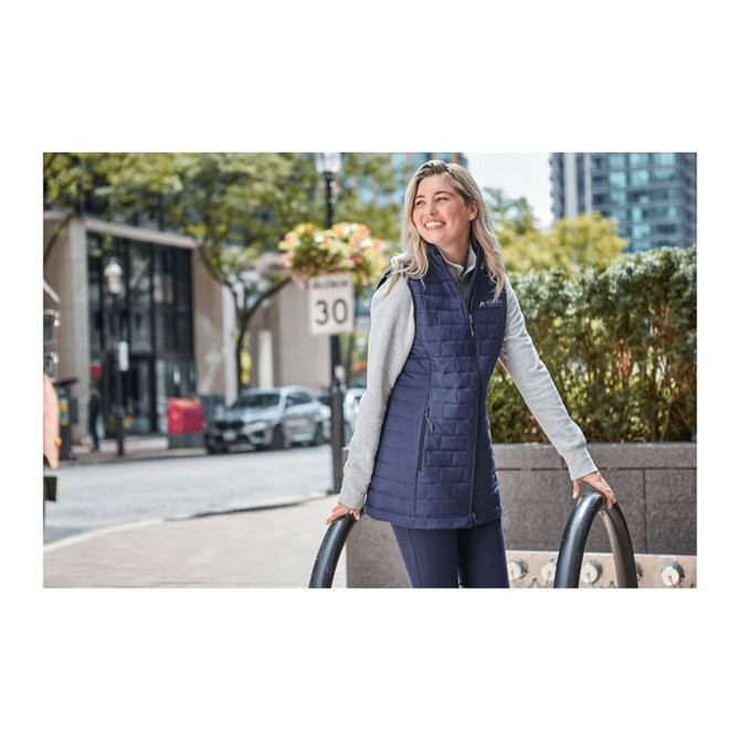A lightweight, insulated puffer vest in navy, featuring a grey hood, displayed on a woman outdoors.