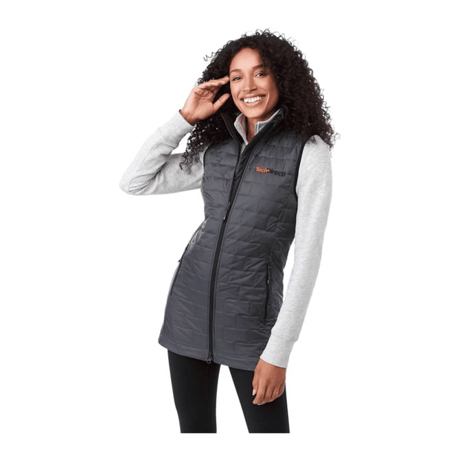 A woman wearing a grey insulated puffer vest over a light grey long-sleeve top, smiling while posing.
