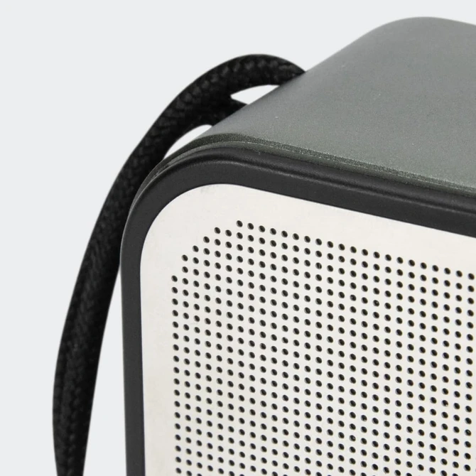 A grey and white portable speaker with a textured surface and a black strap attached.