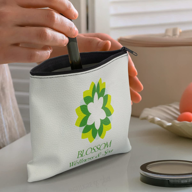 A small white cosmetic bag with a floral design and a zipper, being filled with a lipstick tube.