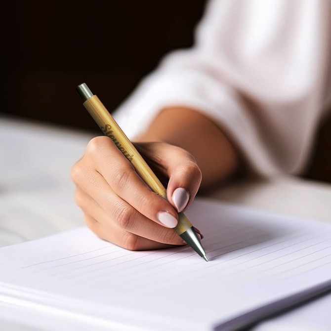 A bamboo pen in hand, featuring a sleek design with green accents, poised above a lined notepad.