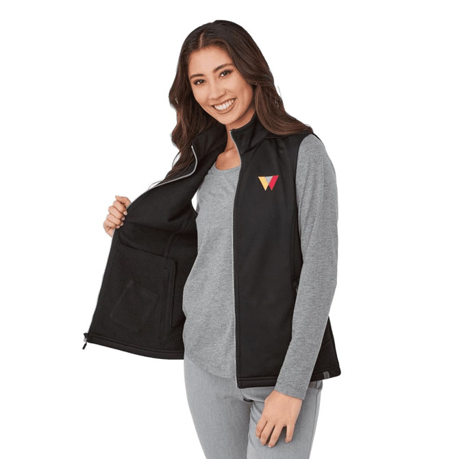 A woman wearing a black eco waterproof softshell vest, featuring a logo on the chest, with an open front.