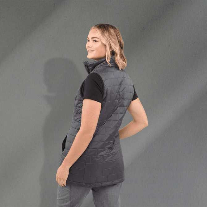 A woman wearing a grey lightweight packable insulated puffer vest, showcasing a side view with a smooth background.
