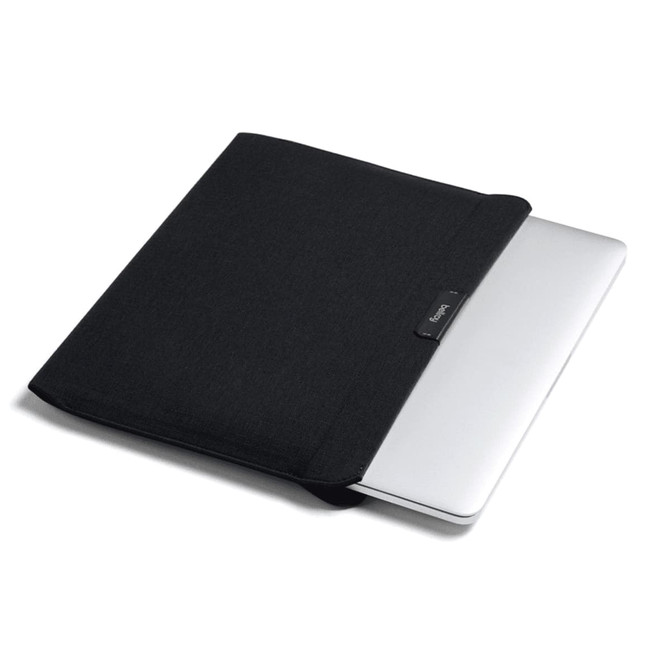 A black laptop sleeve partially covering a silver laptop, featuring a small logo on the front.