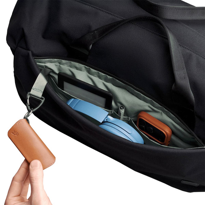 A close-up of a black duffel bag's interior, featuring a blue headset, a gadget, and a brown leather keychain.