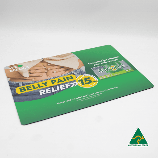 A green counter mat featuring an illustrated design for belly pain relief with a logo, measuring 420mm x 297mm x 1mm.