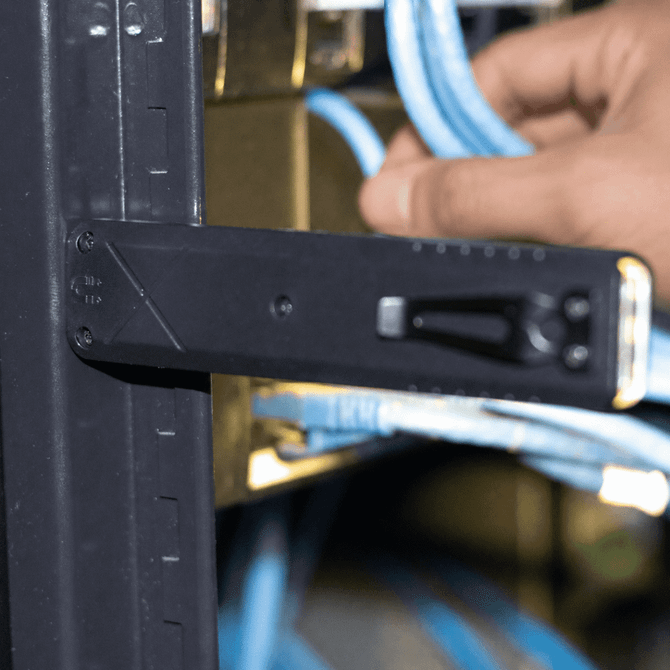 A black tool with a handle and measurement markings, positioned near blue cables in a rack.