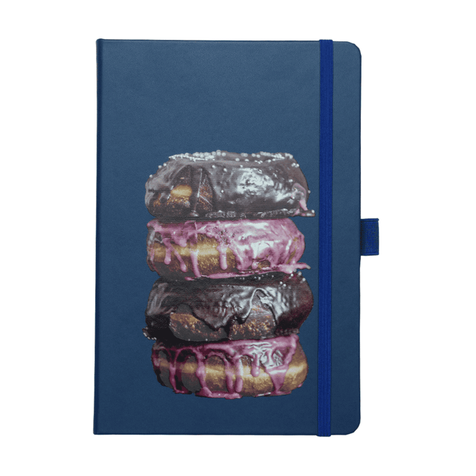 A navy notebook featuring a stack of chocolate and pink iced doughnuts on the cover. The notebook has a logo and an elastic band.