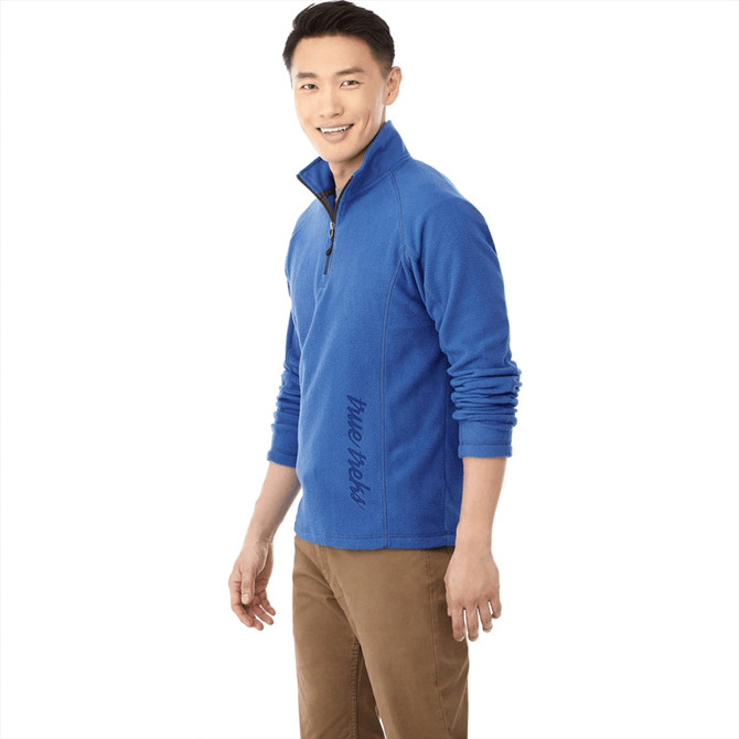 A man wearing a blue polar fleece jumper with a half zip and a logo. The jumper has long sleeves and a casual fit.