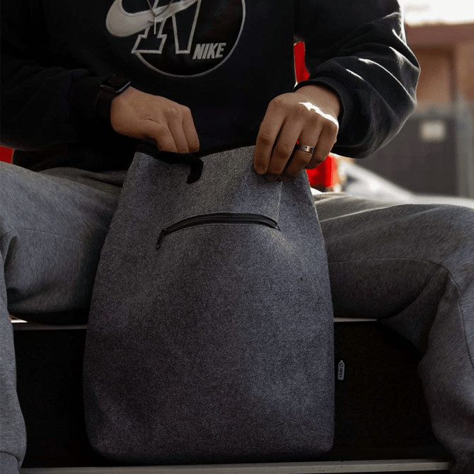 A grey recycled felt cooler tote bag with a zipper pocket, being held by a person wearing casual attire.