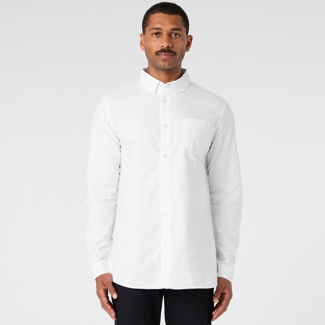 A white button-up Oxford shirt on a model, featuring a chest pocket and long sleeves. The shirt has a logo.