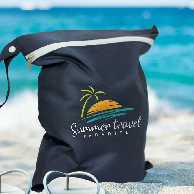 A black wet bag with a logo featuring a sunset and palm tree, sitting on a sandy beach beside flip-flops.