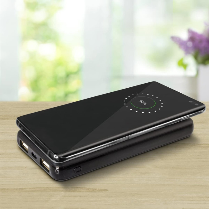A sleek black wireless charging power bank with dual USB ports, placed on a light wooden surface.