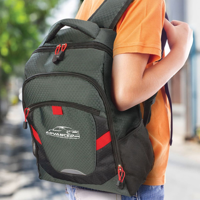 A green backpack with red accents is worn on a person's back, featuring a logo on the front.