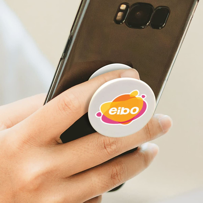A hand gripping a smartphone with a white circular phone grip featuring a multicoloured logo.