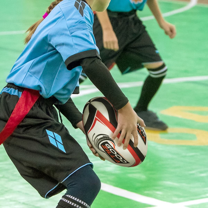 A rugby ball with a distinctive pattern held by a player wearing a blue and black uniform on a green court.