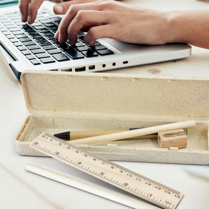 A pencil case in beige with a pencil, sharpener, ruler, and a white pencil, alongside a laptop.
