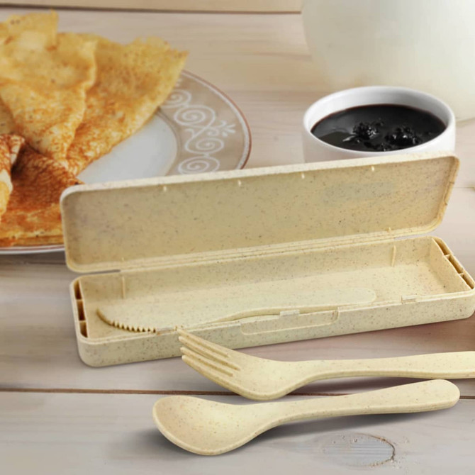 A cutlery set in a beige case, featuring a fork, knife, and a spoon, with a plate of pancakes and a bowl of jam nearby.