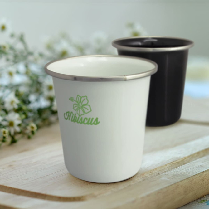 A drink tumbler in white with a green logo and a black tumbler, both with metallic rims, set against a blurred background.