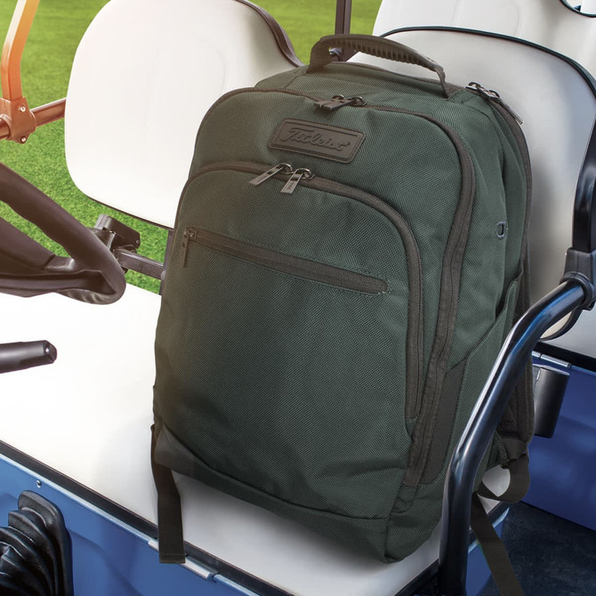 A dark green backpack with a textured finish and a branded logo, placed on a golf cart seat.