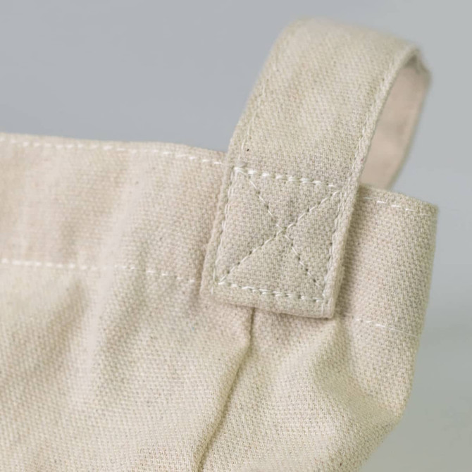 A close-up of a cream cotton shoulder tote bag, featuring a stitched handle with a cross-stitch detail.