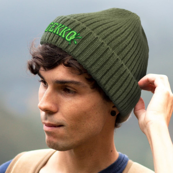 An olive green ribbed beanie with a logo, worn by a person with curly hair.
