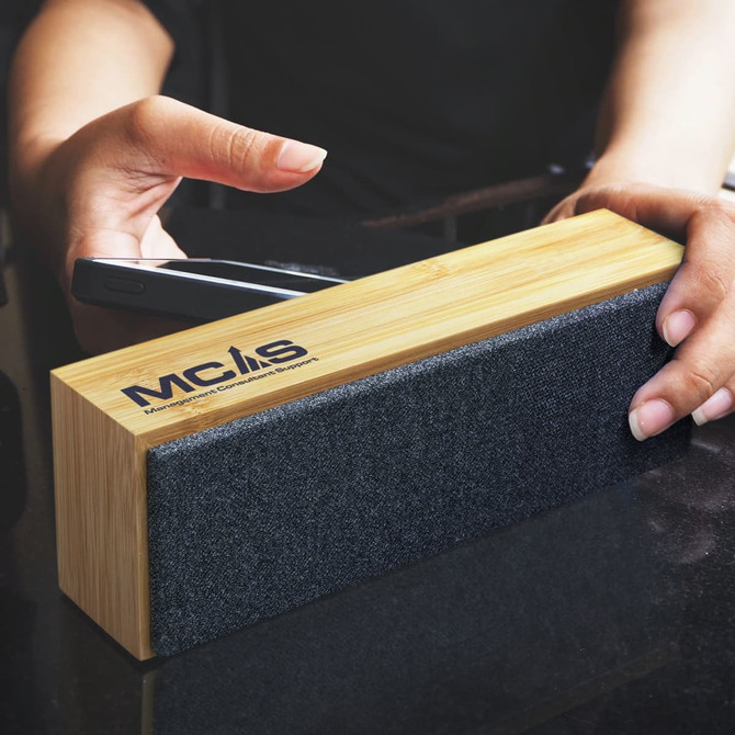A Bluetooth speaker featuring a bamboo design and a dark fabric front, being held near a smartphone.