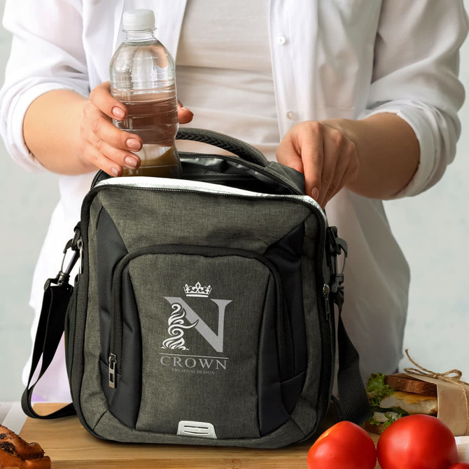 A grey cooler bag being filled with a drink bottle, accompanied by fresh food items on a wooden surface.
