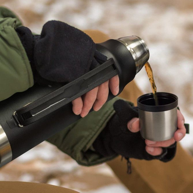 A drink bottle in black with a metal cap, being poured into a stainless steel cup.