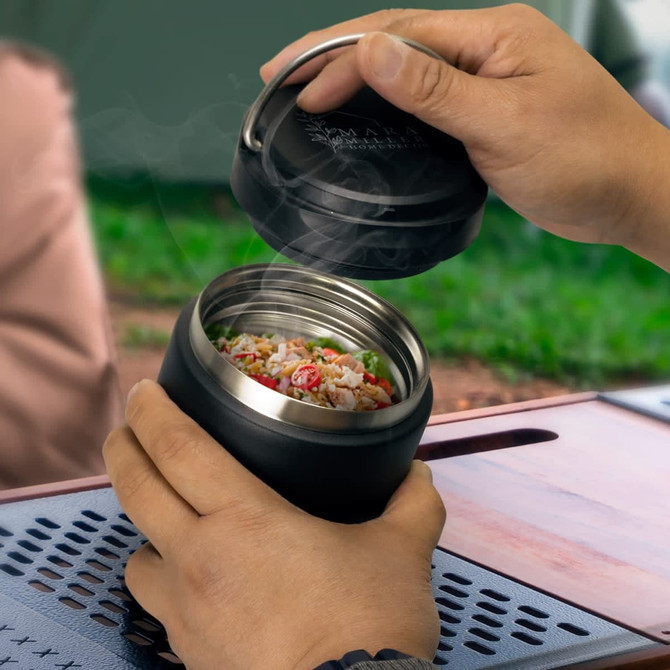 A drink bottle in matte black with a stainless steel interior, being opened to reveal hot food inside.