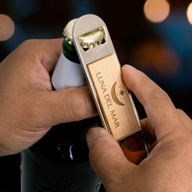 A drink bottle opener featuring a wooden handle and metallic accents, held by a hand over a bottle.