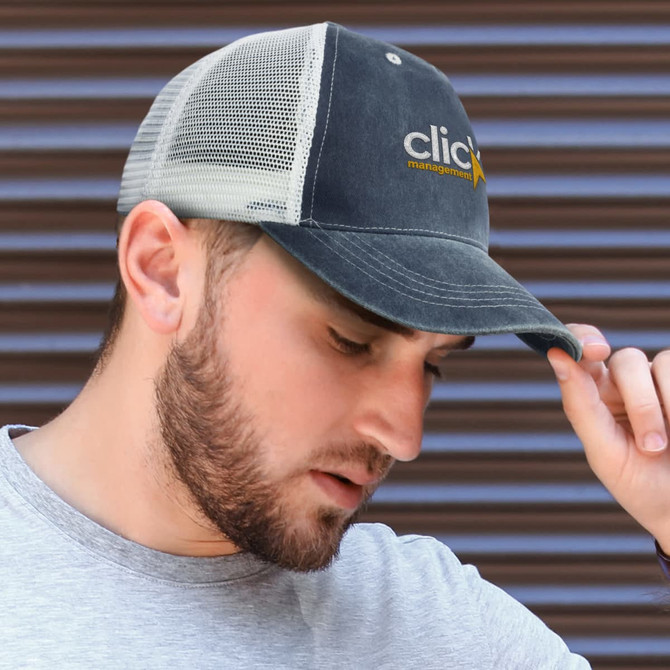 A faded navy trucker cap with a mesh back and a logo on the front, worn by a man with a beard.