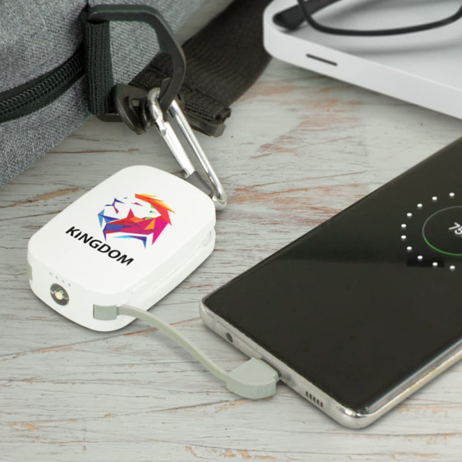 A white power bank with a logo, connected to a smartphone via a grey cable, placed on a wooden surface.