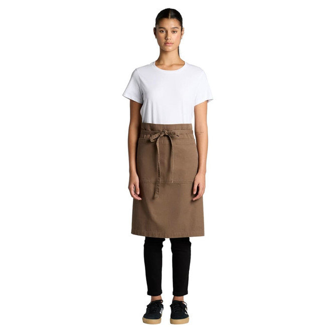 A woman wearing a brown canvas half apron over a white t-shirt and black pants, with a branding logo present.