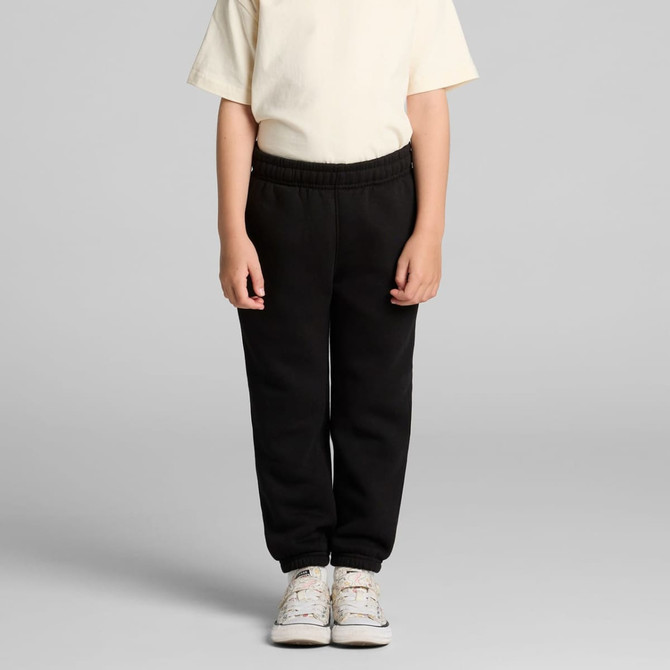 Black youth track pants displayed on a child, paired with a light-coloured t-shirt and casual shoes. It features an elastic waistband.