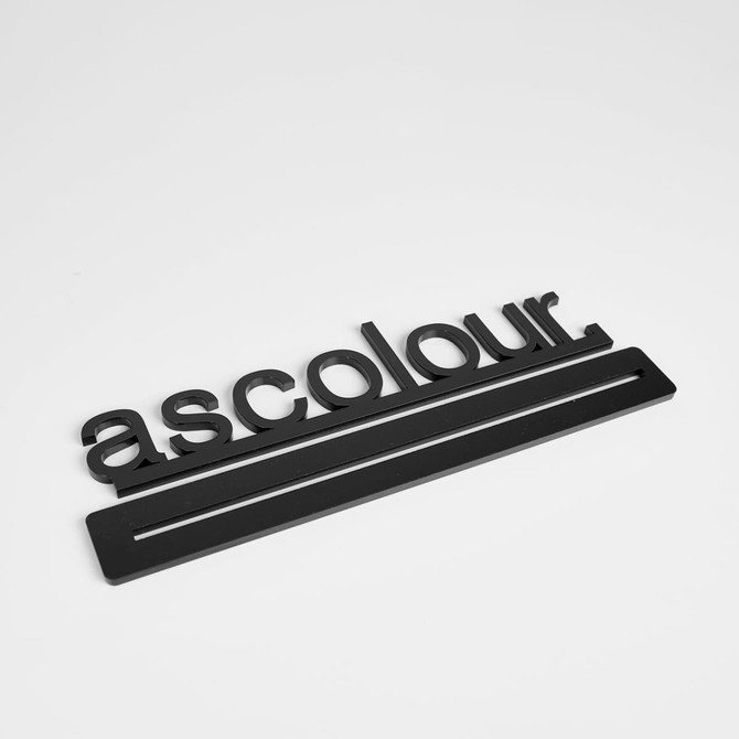 A black promotional product with the word 'ascolour' and a rectangular base, featuring a logo design.
